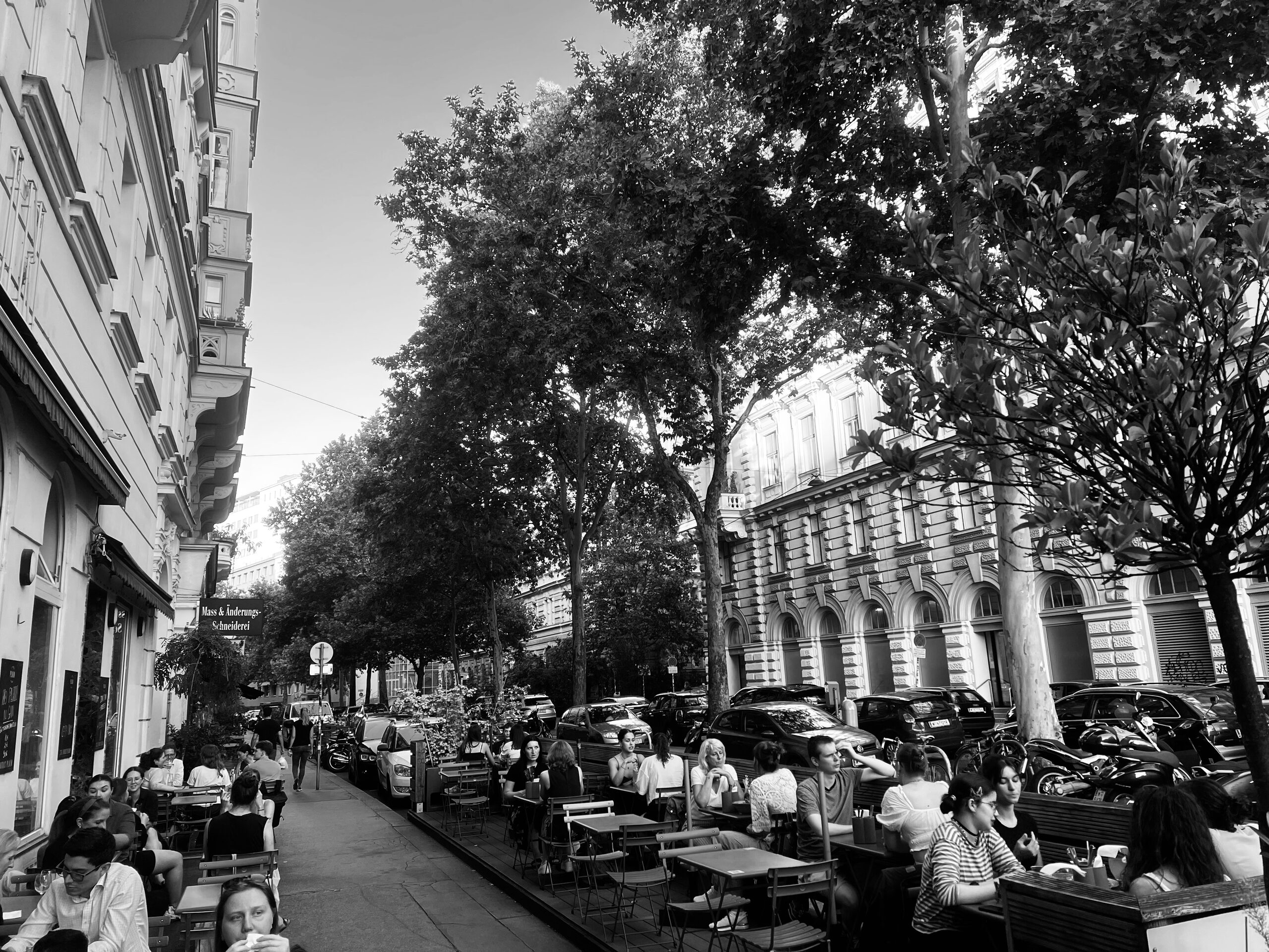 Schanigärten unter den Bäumen: eine Gasse im Grätzel mit Tischen auf beiden Seiten.